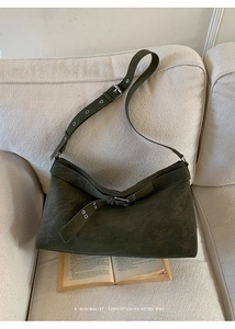 Detail of dark forest green suede tote bag with silver buckle on a cozy beige sofa
