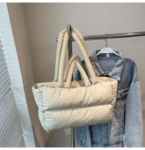 Detail of quilted beige puffer tote bag hanging on a hanger in a minimalist setting