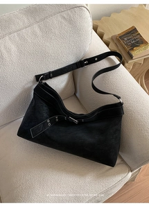 Close-up of black matte tote bag with silver buckle and wide strap on bouclé sofa