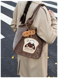 Detail showing the toast dog embroidery and plush croissant charm on the suede tote bag