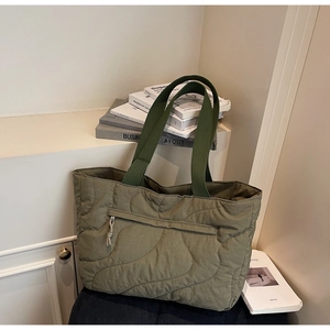Detail of olive green quilted tote bag showing wave stitching and front zipper pocket