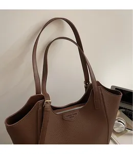 Detail of deep brown tote bag featuring lychee texture leather and adjustable gold buckle