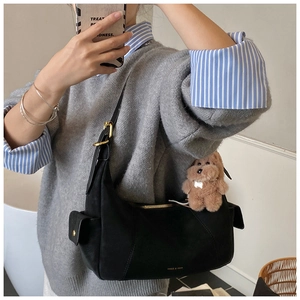 Detail of black suede half-moon shoulder bag featuring a gold zipper and dog plush charm