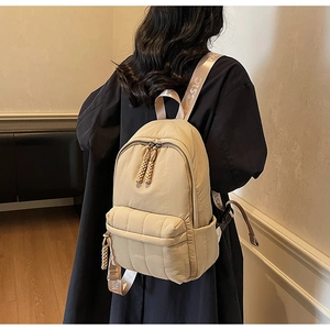 Detailed view of beige quilted backpack showing lettered straps and woven zipper pulls