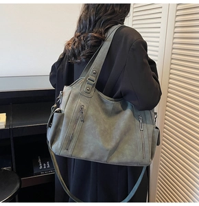 Model wearing a large grey-green tote bag showing side details and textured matte leather