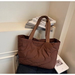 Detail of brown quilted tote bag with wave stitching and branded tag in a cozy setting