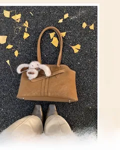Close-up of vintage brown suede tote bag with decorative stitching and a cute rabbit charm