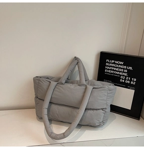 Detailed side view of a light grey quilted puffy tote bag on a white marble surface