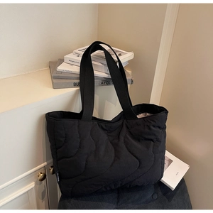 Detail of black quilted tote bag featuring a white brand label and wavy stitching texture