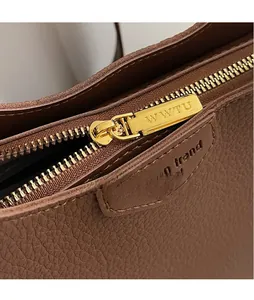 Detail of premium brown pebble leather bag with gold-tone metal zipper and logo hardware