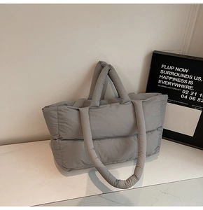 Detail of grey quilted puffer tote bag with dual straps on white marble surface