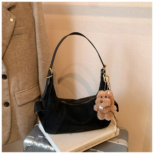 Detail of black suede half-moon shoulder bag with gold hardware and plush dog charm