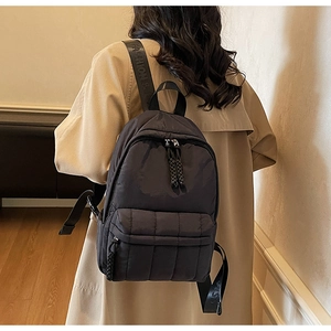 Detail of black quilted nylon backpack with 'FASHION' straps and woven zipper pulls