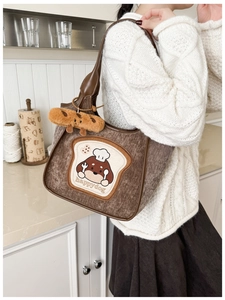 Detail of brown corduroy tote bag with cartoon dog embroidery and plush croissant charm