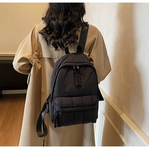 Rear view of a black quilted nylon backpack on a beige trench coat for a stylish look