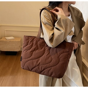 Detail showing wave-pattern quilted fabric and brand tag on a dark brown tote bag