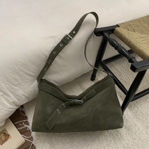 Detail of dark green suede tote bag with silver metal buckles in a home setting