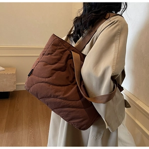 Detail of brown quilted puffer tote bag with side brand label and wide shoulder strap