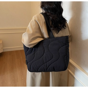 Detailed view of black quilted tote bag showing wave stitching and branded side label