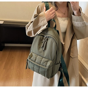 Detail of army green quilted backpack featuring woven zipper pulls and branded straps