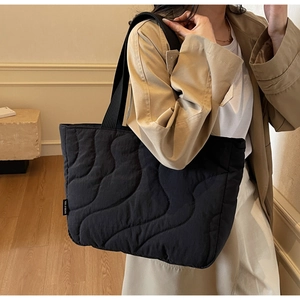 Detailed shoulder view of a black quilted tote bag with wavy stitching and side logo tag