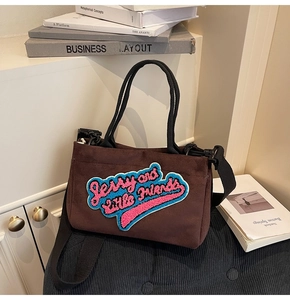 Détail du sac à bandoulière en daim marron avec broderie colorée au logo Jerry