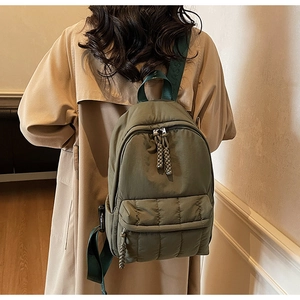 Detail of dark green nylon backpack featuring quilted front pocket and woven zipper pulls