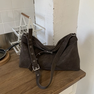 Close-up of brown suede tote bag featuring metallic eyelets and adjustable buckle strap