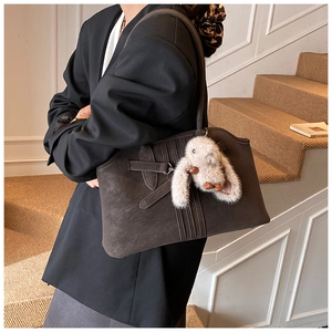 Deep brown matte leather tote bag with stylish strap detail and plush rabbit pendant