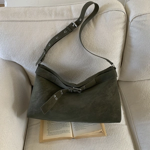 Close-up of olive green suede tote bag with metal eyelets and belt detail on a sofa