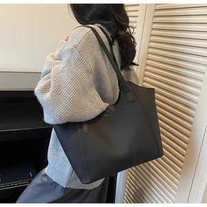 Close-up of black leather tote bag with pebble texture and slim shoulder straps on model