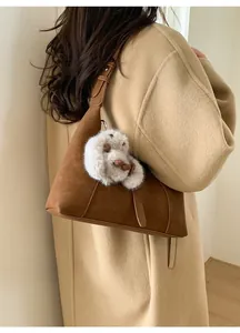 Detail view of a brown matte leather crossbody bag featuring a white plush bunny charm
