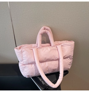 Pink quilted puffer tote bag with puffy handles and long strap on a black bench decor
