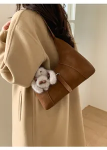 Close-up of brown suede shoulder bag with plush rabbit charm on winter wool coat