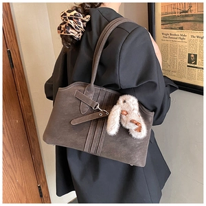 Detail of dark brown faux suede tote bag featuring a plush rabbit pendant and stitching