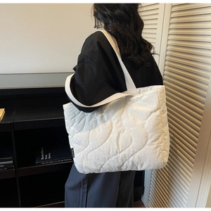 Detail view of white quilted shoulder bag showing wavy padded stitching and side brand label