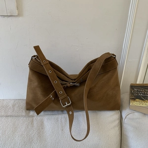 Detail of a brown suede shoulder bag with adjustable buckle strap and silver eyelets