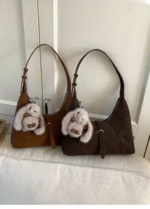 Close-up of suede shoulder bags in caramel and dark brown with plush rabbit charms