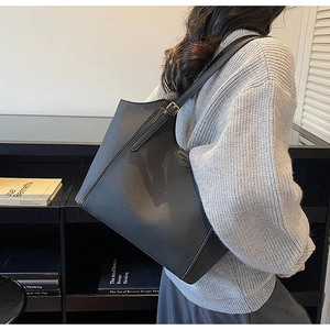 Close-up of black lychee grain tote bag showing metal buckle and narrow shoulder strap
