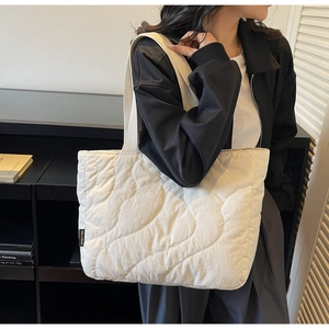 Close-up of cream quilted tote bag with wavy stitching and brand label detail
