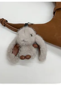 Detail of plush rabbit charm featuring grey faux fur, brown leather accents, and silver clip