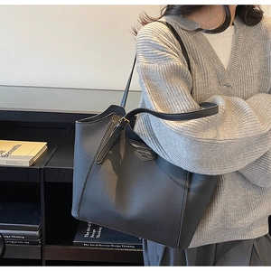 Detail of dark grey lychee leather tote bag with a shield-shaped fashion brand patch