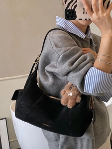 Black suede half-moon underarm bag with gold zipper and plush bear charm on strap