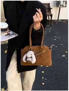 Brown suede shoulder bag with leather crisscross straps and white plush rabbit charm