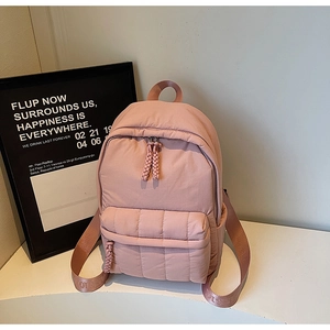 Detail of light pink quilted backpack featuring soft puffer material and woven zipper pull