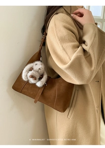 Brown hobo bag with matte texture and white plush bunny charm on camel wool coat