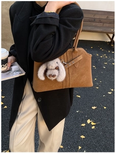 Close-up of brown suede tote bag with decorative straps and grey plush rabbit pendant