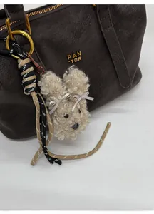 Detail of beige fleece animal bag charm with white bows on a brown leather handbag