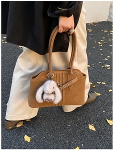 Detail of dark brown suede tote bag featuring metallic buckle and plush rabbit charm