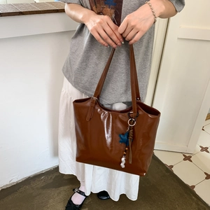 Detail of deep brown glossy leather tote bag with unique star and peanut charms on a model